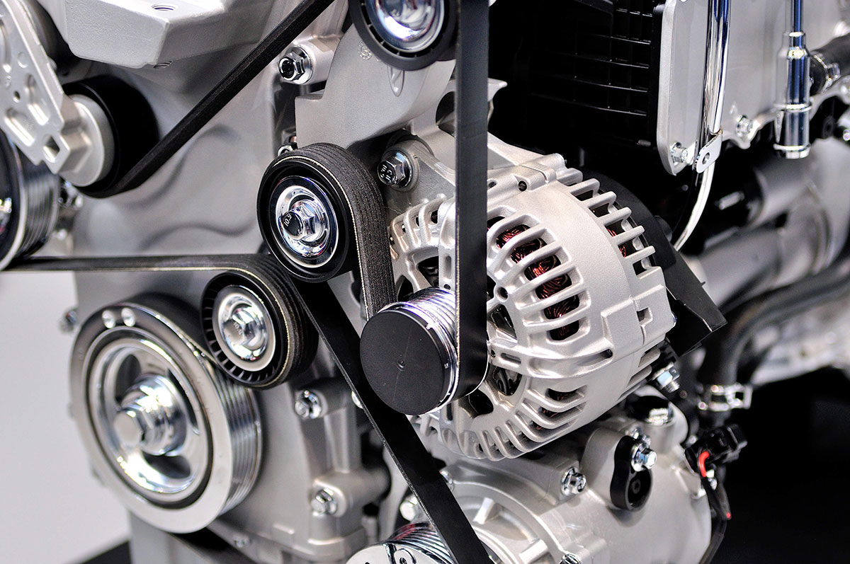 Serpentine belt routed around the alternator and idler pulleys on the front of an engine.