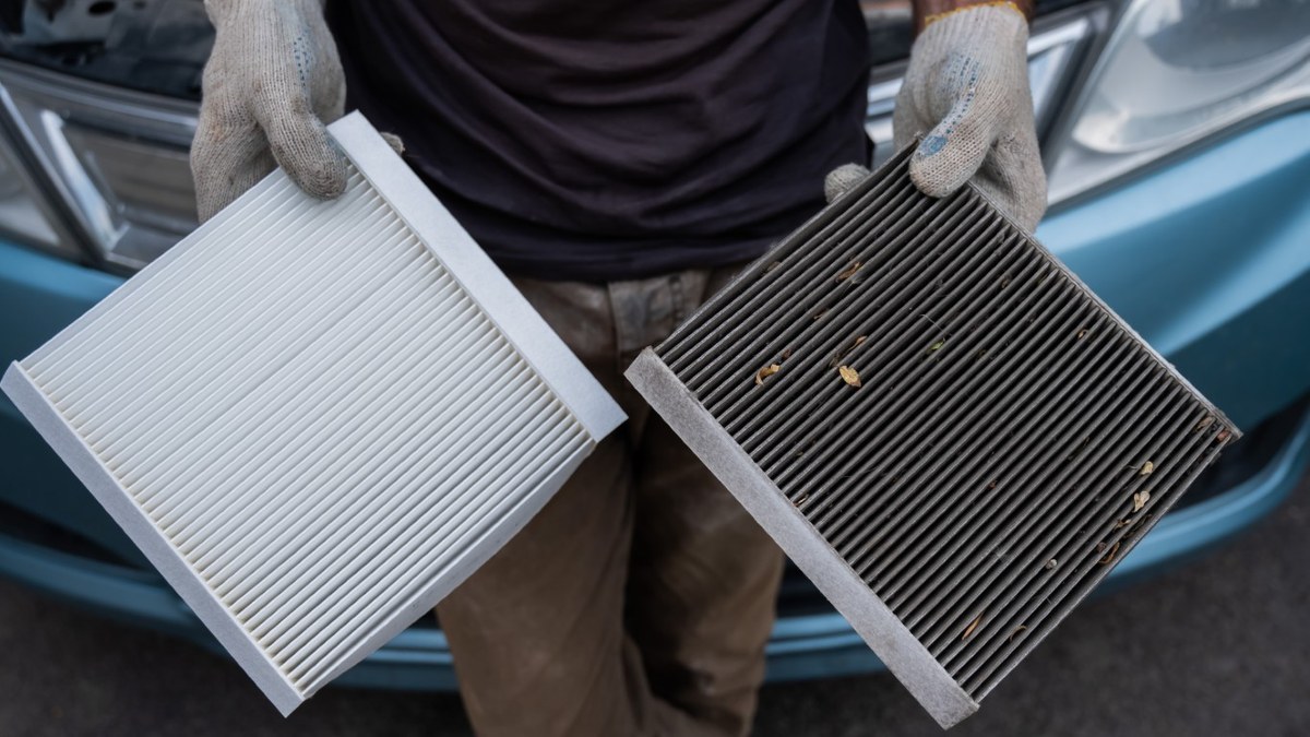 A clean white cabin air filter held next to a grey one clogged with road debris.