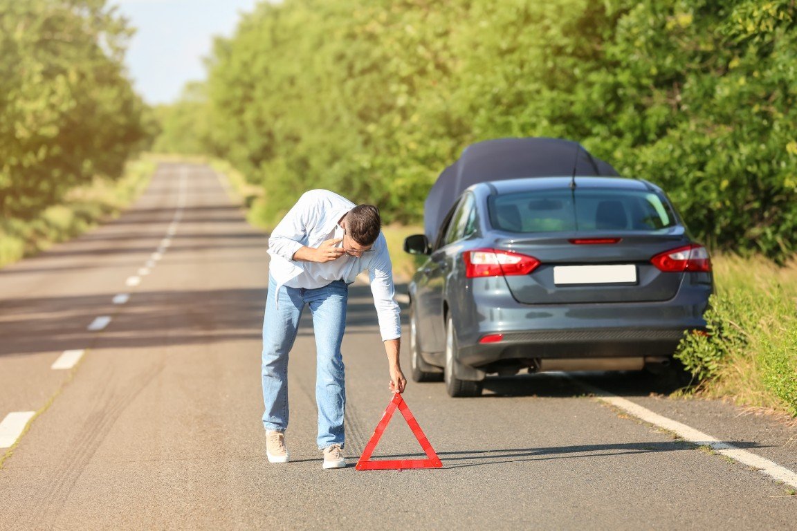 Driver setting out a reflective warning triangle behind a vehicle on the roadside