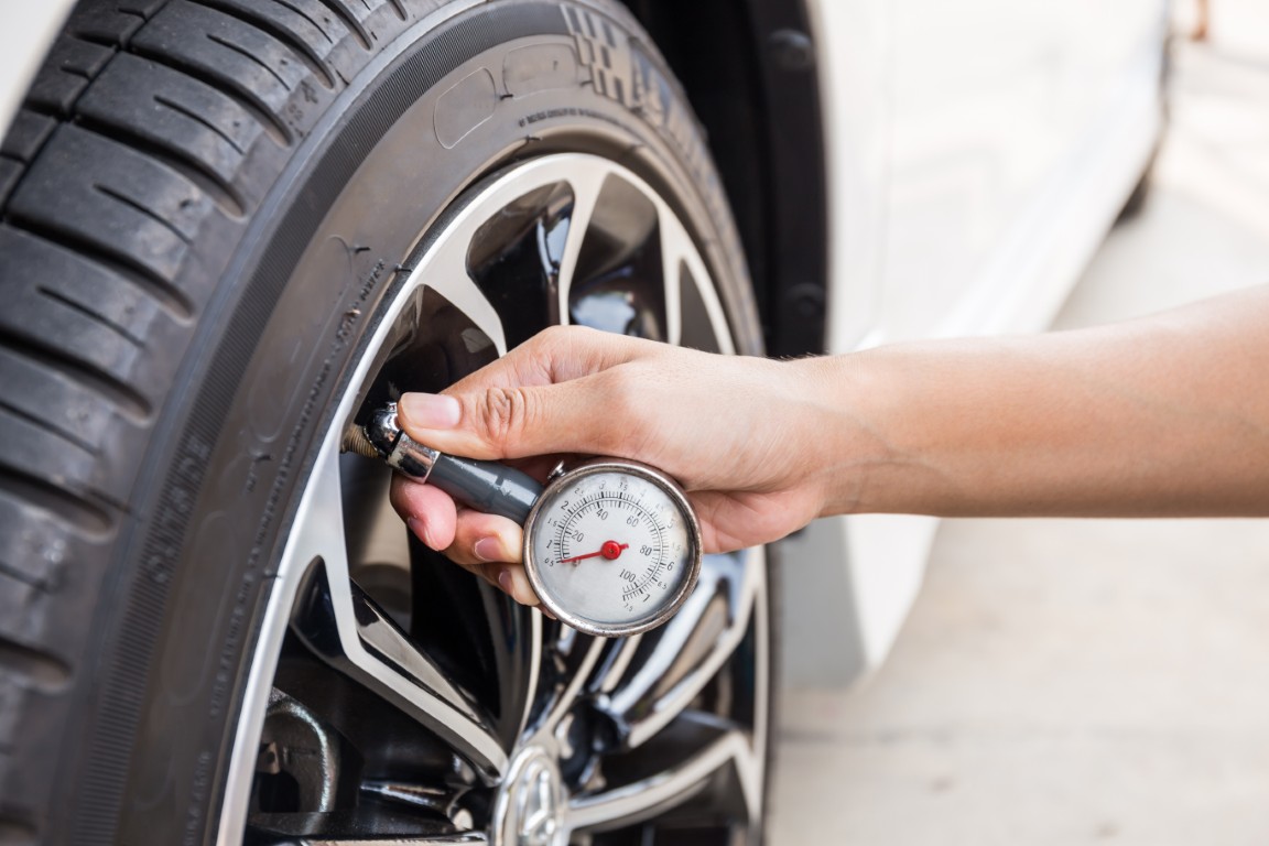Hand holding a dial tire pressure gauge against a tire's valve stem.