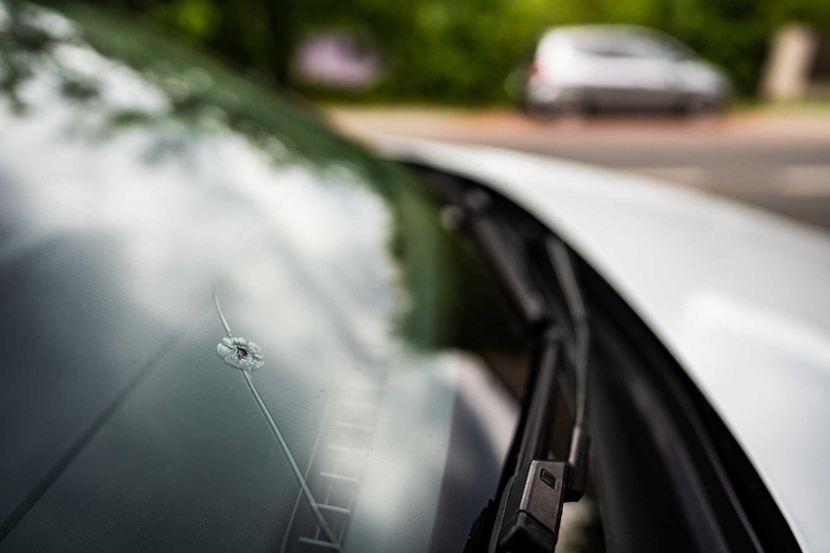 Rock chip with radiating cracks in a car windshield near the wiper