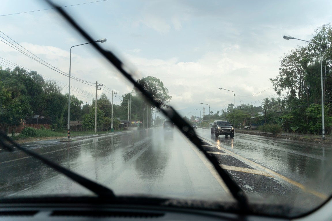 View through a rain-covered windshield of a wet road with the wiper blade mid-sweep.